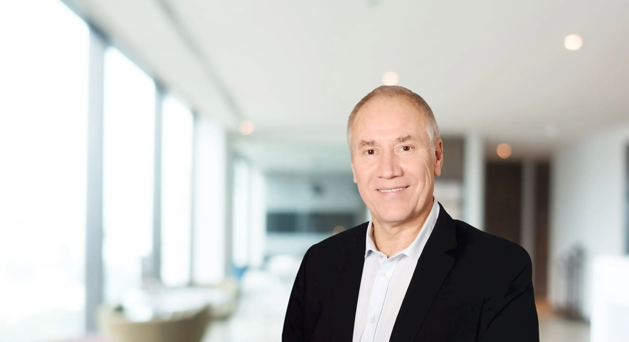 Thomas Gillar steht in einem lichtdurchfluteten Büro und lächelt in die Kamera